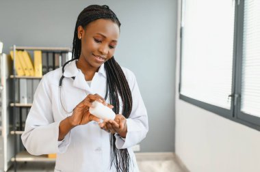 Gülümseyen Afrikalı kadın doktor ya da eczacının, renkli kabarcıkları haplarla tutarken, eczanede ya da hastanede kameraya gösterirken, yatay çekimini kapat.