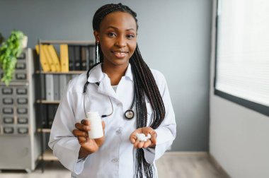 Gülümseyen Afrikalı kadın doktor ya da eczacının, renkli kabarcıkları haplarla tutarken, eczanede ya da hastanede kameraya gösterirken, yatay çekimini kapat.