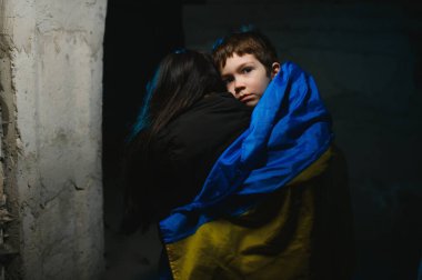 Üzgün anne oğluna sarılıyor, ikisi de siyah arka planda Ukrayna ulusal renkleri giyiyor..