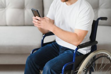 Tekerlekli sandalyedeki genç ve mutlu girişimci evdeki akıllı telefondan mesaj okuyor..