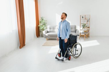 Evde tekerlekli sandalyeden kalkmaya çalışan engelli genç adam, boşluğu kopyalamaya çalışıyor..