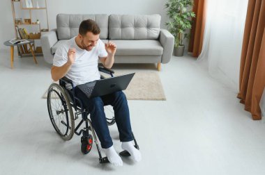 Evde çalış. Felç olmuş erkek diz üstü bilgisayar tutuyor ve ekrana bakarken yüzünde gülümsemeyi sürdürüyor.