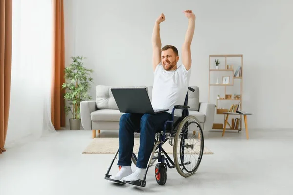 在家工作 膝上抱着笔记本电脑 望着屏幕时面带微笑的瘫痪男性 — 图库照片