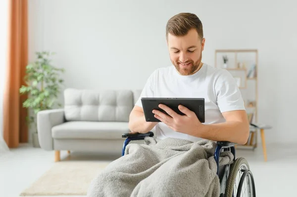 坐在轮椅上的人在家里用平板电脑 积极的退休男性 身体残疾在触摸板上浏览网页 在室内观看视频 — 图库照片