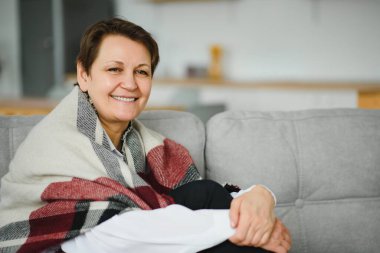 Evdeki kanepede ekoseli yaşlı bir kadının portresi.