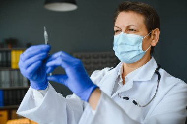 Doktor üniformalı kadın doktor ya da bilim adamlarının yakından incelediği yüz maskesi takan laboratuarda sıvı aşı şişesi, koronavirüs ya da COVID-19 konsepti tutan kişi..