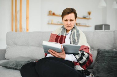 Evde kitap okuyan kıdemli bir kadın..