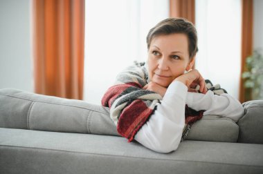 Olgun Kadın. Evdeki koltukta oturan sağlıklı, orta yaşlı, güzel bir kadın. Güzellik ve Rahatlık Konsepti.