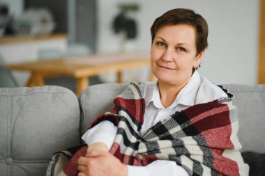 Olgun Kadın. Evdeki koltukta oturan sağlıklı, orta yaşlı, güzel bir kadın. Güzellik ve Rahatlık Konsepti.