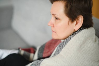 Evdeki kanepede ekoseli yaşlı bir kadının portresi.