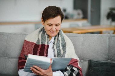 Evdeki kanepede ekoseli yaşlı bir kadının portresi.