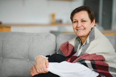 Olgun Kadın. Evdeki koltukta oturan sağlıklı, orta yaşlı, güzel bir kadın. Güzellik ve Rahatlık Konsepti.