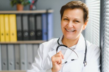 Orta yaşlı kadın doktor portresi boynunda steteskop olan beyaz bir doktor önlüğü giyiyor..