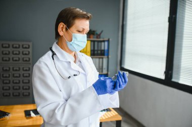 Doktor üniformalı kadın doktor ya da bilim adamlarının yakından incelediği yüz maskesi takan laboratuarda sıvı aşı şişesi, koronavirüs ya da COVID-19 konsepti tutan kişi..