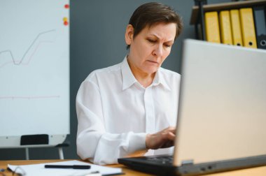 Orta yaşlı iş kadını profesyonel eğitim sınıfını izliyor, bilgisayarlı bilgisayarda uzaktan kumanda kullanıyor, ofisten uzaklığı öğreniyor, konferans için sanal sohbet çağrısı yapıyor..