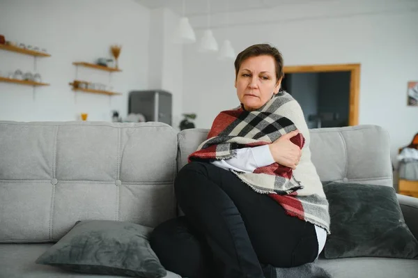 五十多岁生病的冻僵女人坐在客厅的沙发上 浑身暖烘烘地打喷嚏 流鼻涕感觉不健康 季节性感冒 免疫系统弱化 — 图库照片