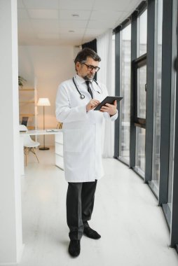 Mutlu, kendine güvenen, yaşlı, profesyonel doktor ayakta duruyor. Gülümseyen yetişkin doktor, güvenilir başarılı terapist beyaz laboratuvar önlüğü ve steteskop giyiyor, portre.