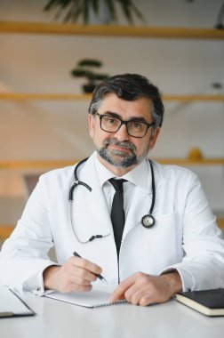 Ciddi profesyonel kıdemli yaşlı doktor iş yerindeki tıbbi belgeleri kontrol ediyor. Hasta teşhisini ya da hastane raporunu inceleyen, tıbbi form okuyan konsantre yaşlı bir doktor..