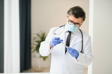 Üniformalı, maskeli bir erkek doktor, şırınga tutan tıbbi eldivenler şırıngaya hazırlanan şişe 19 Corona virüsü aşısı. Coronavirus aşılama grip aşısı