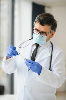 Üniformalı, maskeli bir erkek doktor, şırınga tutan tıbbi eldivenler şırıngaya hazırlanan şişe 19 Corona virüsü aşısı. Coronavirus aşılama grip aşısı