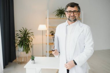 Sağlık görevlisinin portresi. Laboratuvar önlüğü giyen ve özel klinikte duran yaşlı bir erkek doktorun resmi..
