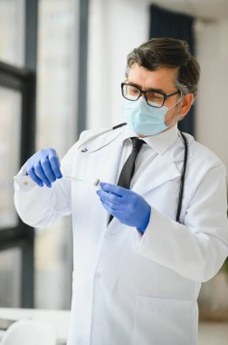 Üniformalı, maskeli bir erkek doktor, şırınga tutan tıbbi eldivenler şırıngaya hazırlanan şişe 19 Corona virüsü aşısı. Coronavirus aşılama grip aşısı
