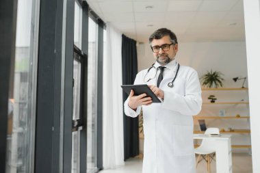 Mutlu, kendine güvenen, yaşlı, profesyonel doktor ayakta duruyor. Gülümseyen yetişkin doktor, güvenilir başarılı terapist beyaz laboratuvar önlüğü ve steteskop giyiyor, portre.