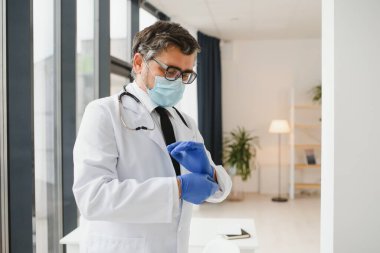 Koruyucu maskeli erkek doktor klinikte eldiven takıyor.