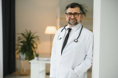 Mutlu, kendine güvenen, yaşlı, profesyonel doktor ayakta duruyor. Gülümseyen yetişkin doktor, güvenilir başarılı terapist beyaz laboratuvar önlüğü ve steteskop giyiyor, portre.