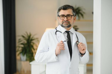 Mutlu, kendine güvenen, yaşlı, profesyonel doktor ayakta duruyor. Gülümseyen yetişkin doktor, güvenilir başarılı terapist beyaz laboratuvar önlüğü ve steteskop giyiyor, portre.
