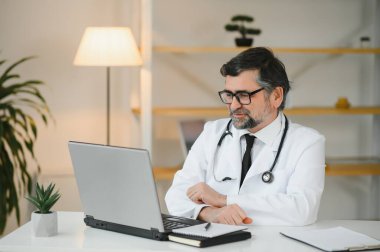 Tıp bürosunda dizüstü bilgisayar kullanan ciddi bir doktorun portresi..