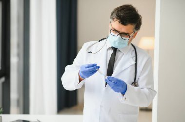 Üniformalı, maskeli bir erkek doktor, şırınga tutan tıbbi eldivenler şırıngaya hazırlanan şişe 19 Corona virüsü aşısı. Coronavirus aşılama grip aşısı