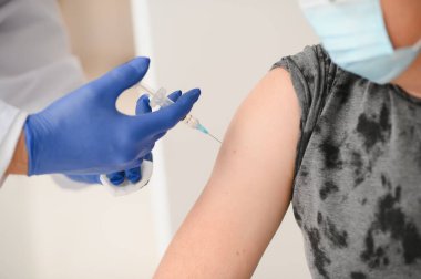 İlaç, aşı ve sağlık konsepti - virüs hastalığından korunmak için yüz koruyucu maske takan doktor ve şırınga ile erkek hastaya aşı enjekte ediliyor