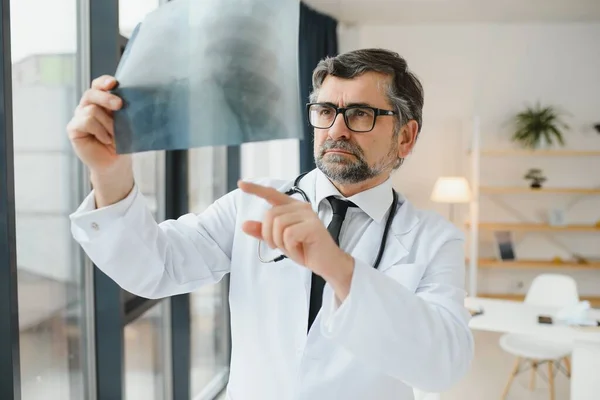 older man doctor examines x-ray image of lungs in a clinic.