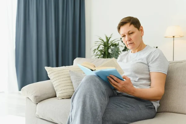 一个幸福的成熟女人 在沙发上放松和阅读一本书在现代家庭中的肖像 — 图库照片