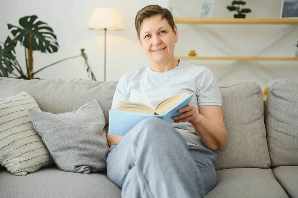 中年家庭主妇坐在沙发上看书 空闲时间退休 — 图库照片