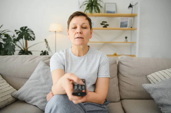 Middle Aged Woman Sitting Sofa Turning Remote Control — стоковое фото