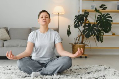 Yetişkin bir kadın evde fitness egzersizi yapıyor. Kıdemli kadın esneme egzersizleri yapıyor. Olgun kadın yoga pozları veriyor..