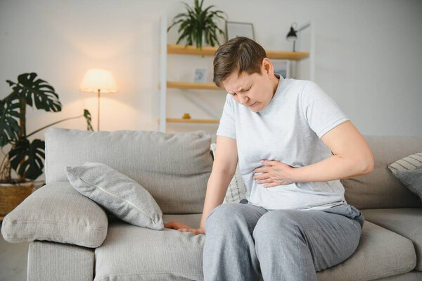Sick upset middle aged lady hold belly suffer from abdomen ache concept, mature old adult woman feel morning pain hurt in stomach abdominal gastritis pancreatitis diarrhea problem symptom sit on bed