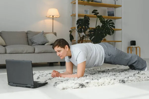 Middle aged woman in plank position keeps fit in her home - Elderly person has fun doing sports - mental and physical well-being concept.