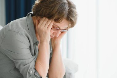 Yaşlı bir kadının baş ağrıları olur, elleriyle kafasına dokunur, baş dönmesi ve migren belirtileri gösterir.