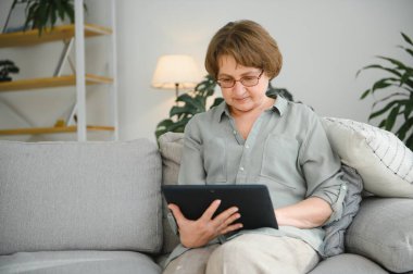 Kanepedeki dijital tabletine bakıp gülen son sınıf öğrencisi kadın..