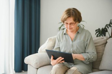 Kanepedeki dijital tabletine bakıp gülen son sınıf öğrencisi kadın..