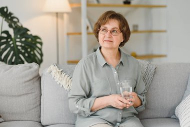 Yaşlı kadın kanepede oturuyor ve evde hap alıyor. İlaç kullanan emekliler..