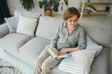 Kitap ile kanepede oturan rahat kadın kıdemli portresi.