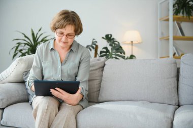 Kanepedeki dijital tabletine bakıp gülen son sınıf öğrencisi kadın..