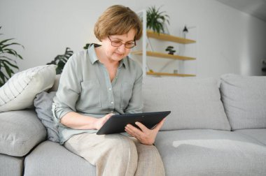 Kanepedeki dijital tabletine bakıp gülen son sınıf öğrencisi kadın..