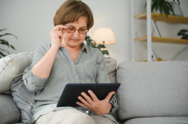 Kanepedeki dijital tabletine bakıp gülen son sınıf öğrencisi kadın..