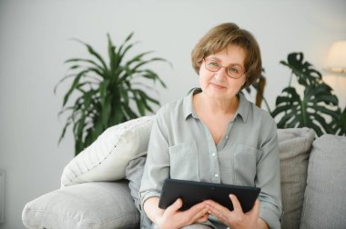 Kanepedeki dijital tabletine bakıp gülen son sınıf öğrencisi kadın..