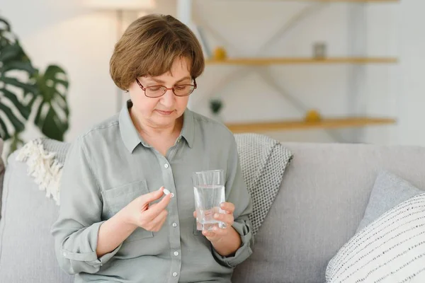 成熟的中年妇女持有丸和杯水服用止痛药 以缓解疼痛 药物补充维生素 抗生素药物 老年人概念的药物 特写视图 — 图库照片